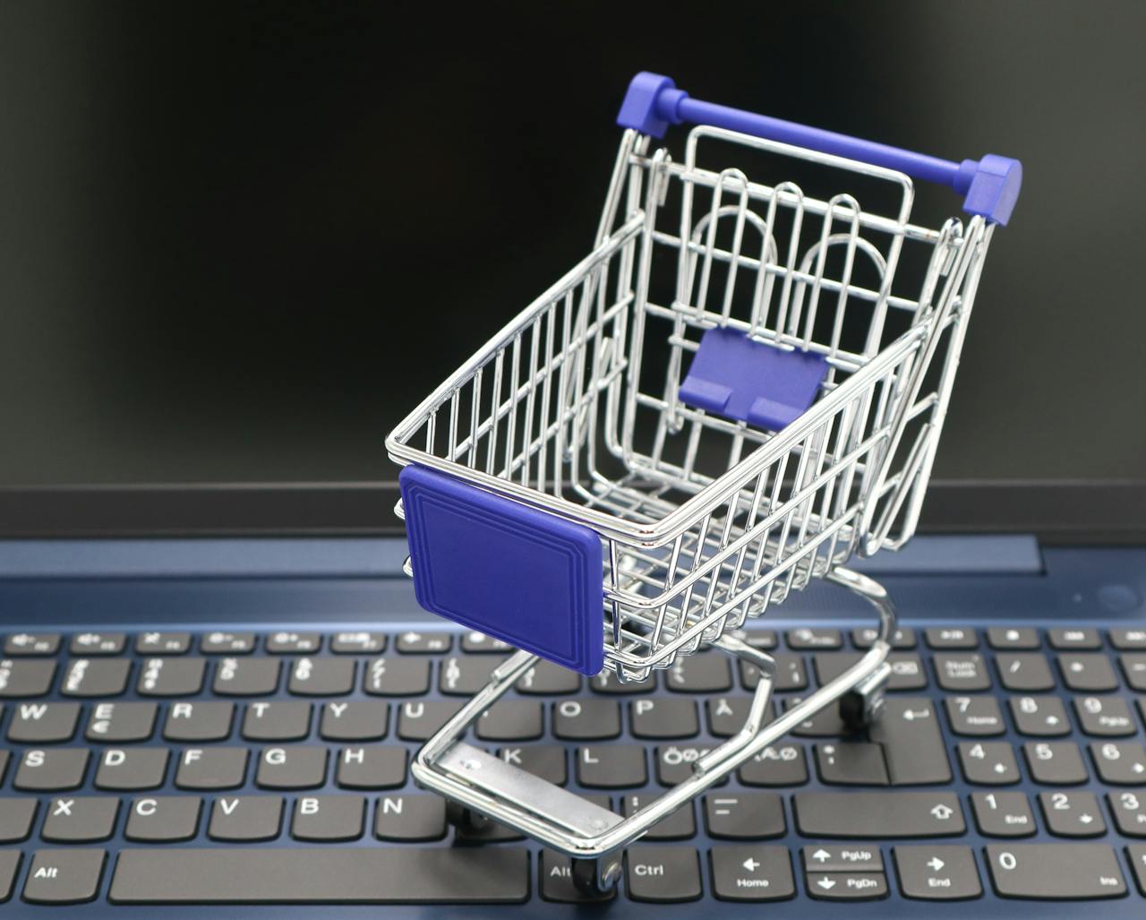 services-02 A mini shopping cart placed on a laptop keyboard, symbolizing online shopping and digital retail.